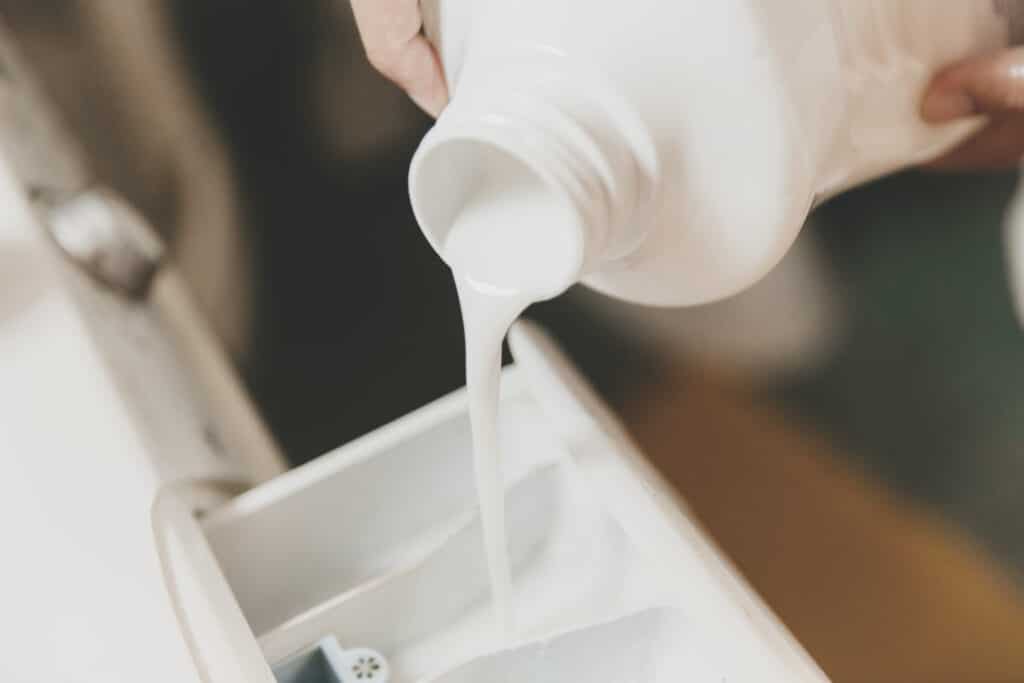 Noen heller vaskemiddel fra en plastflaske opp i en vaskemaskin.
